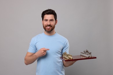 Smiling man showing chessboard with game pieces on light grey background