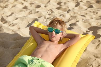 Photo of Cute little child with inflatable mattress lying at sandy beach on sunny day