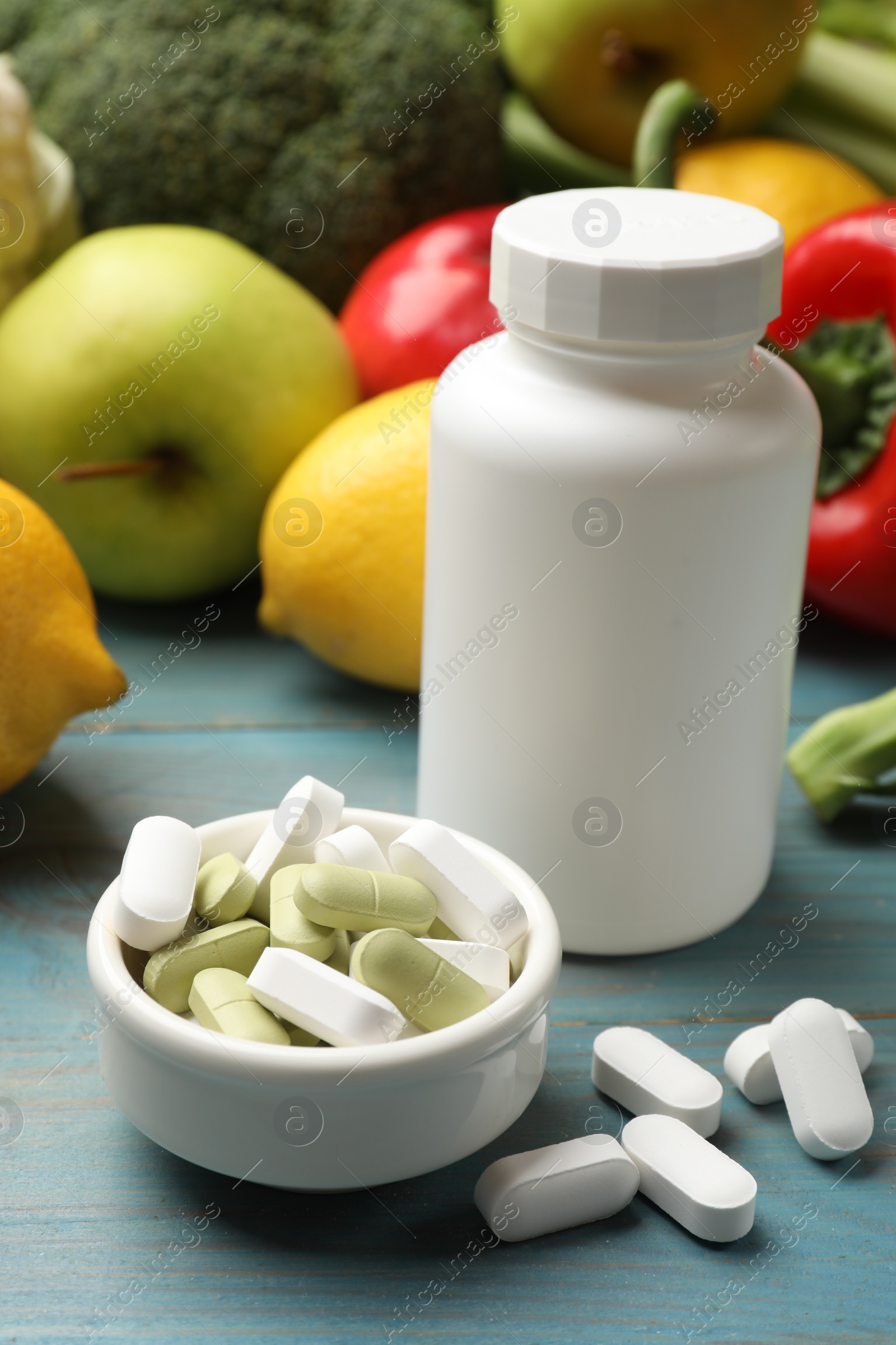 Photo of Dietary supplements. Blank white bottle and bowl with different pills near food products on light blue wooden table, closeup