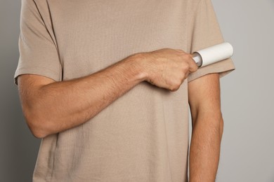 Man using lint roller on light grey background, closeup