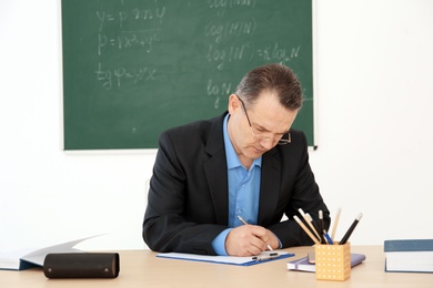 Male teacher working at table in classroom