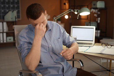 Photo of Overworked man with headache trying to take  pill in office