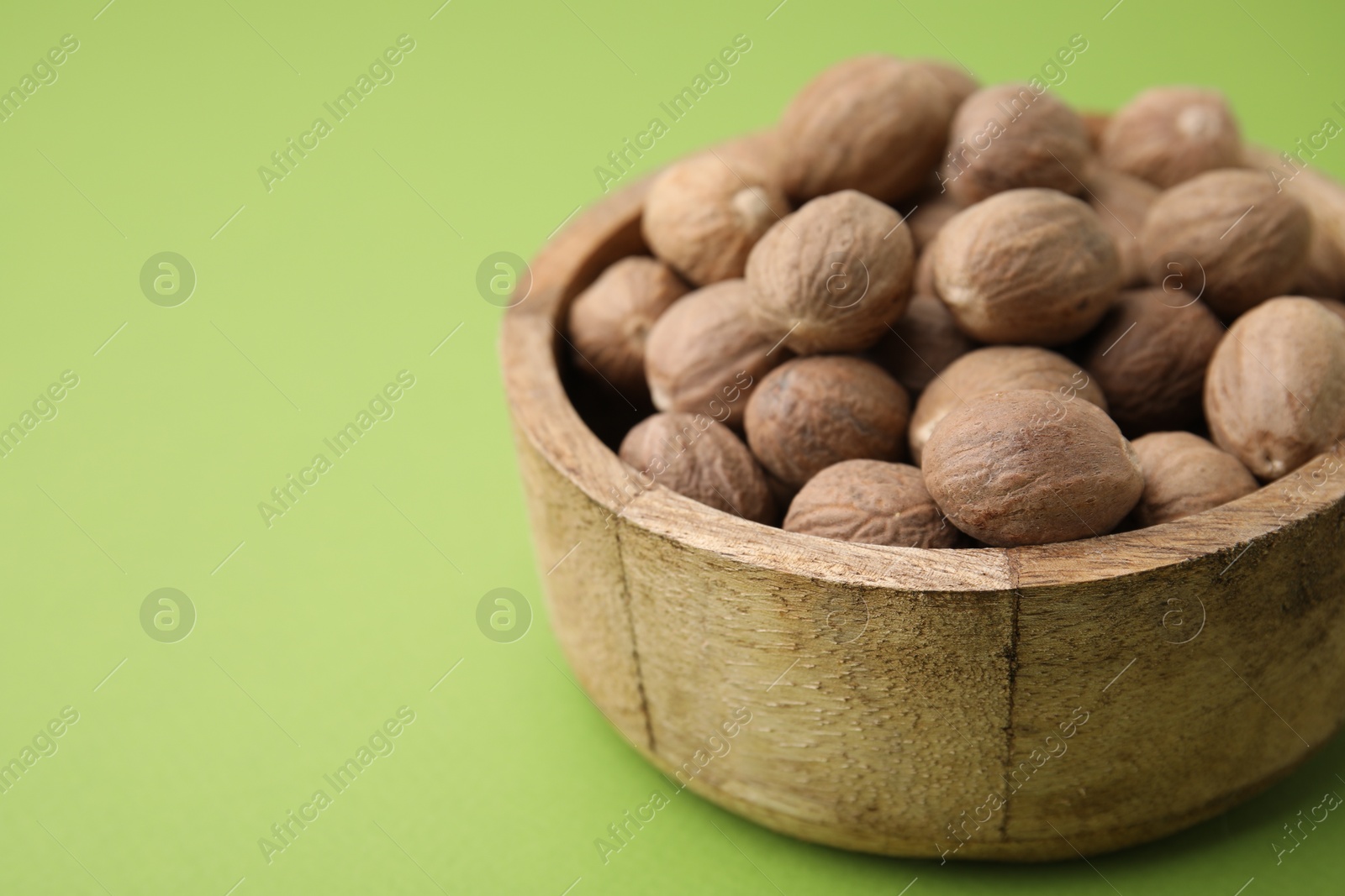 Photo of Whole nutmegs in bowl on light green background, closeup. Space for text