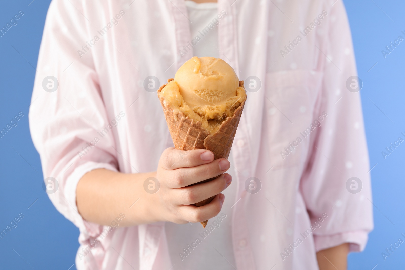 Photo of Woman holding yellow ice cream in wafer cone on light blue background, closeup