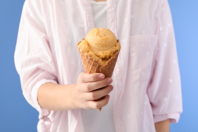 Woman holding yellow ice cream in wafer cone on light blue background, closeup