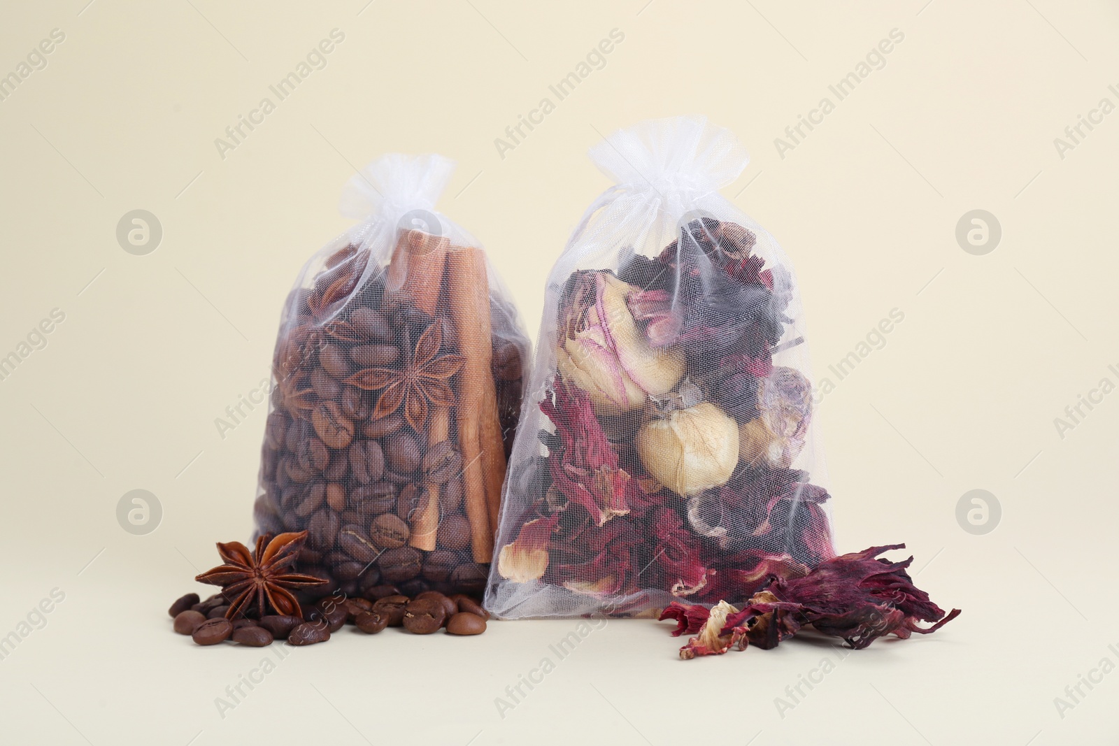 Photo of Scented sachets with dried roses, coffee beans, anise and cinnamon on beige background