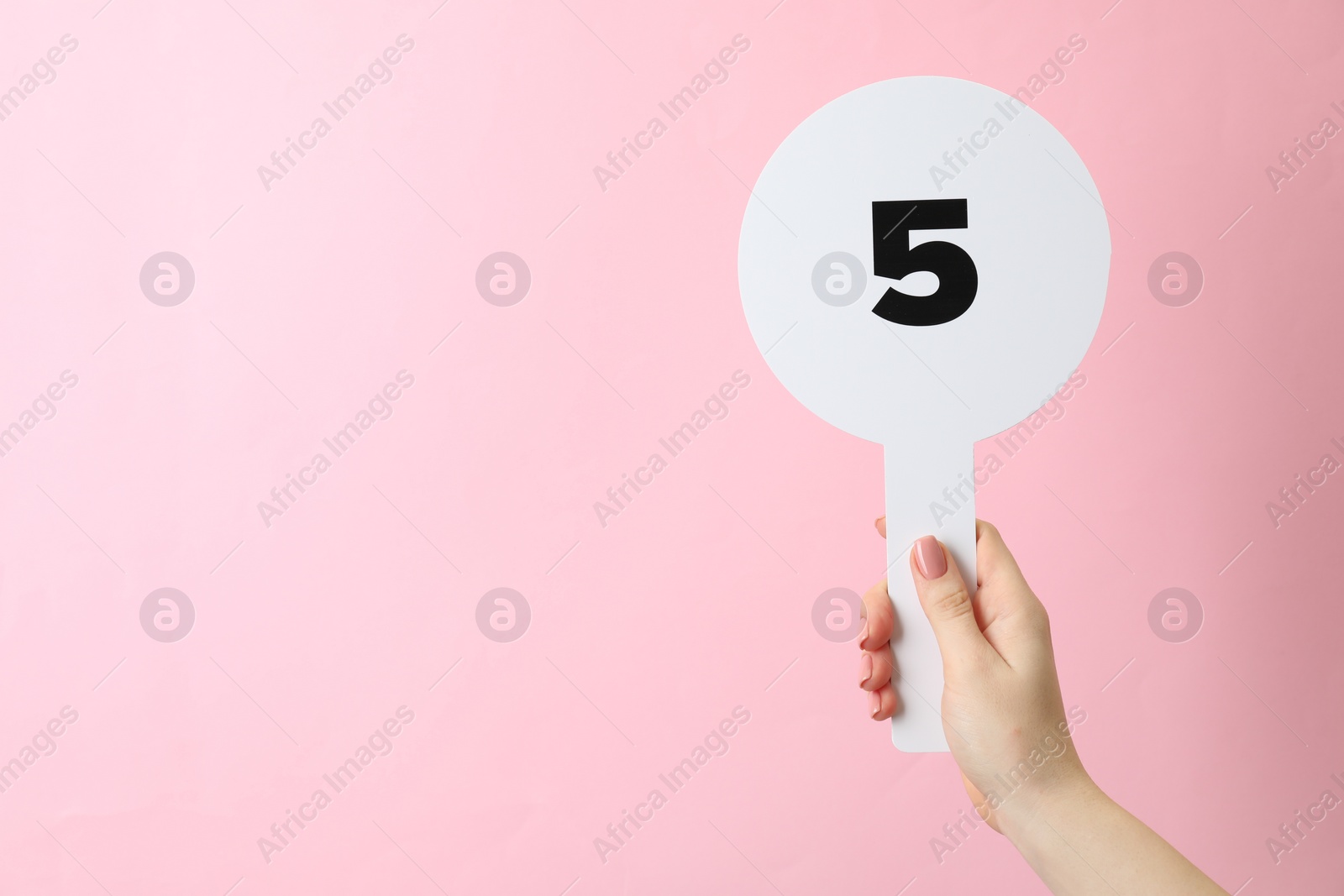 Photo of Woman holding auction paddle with number 5 on pink background, closeup. Space for text