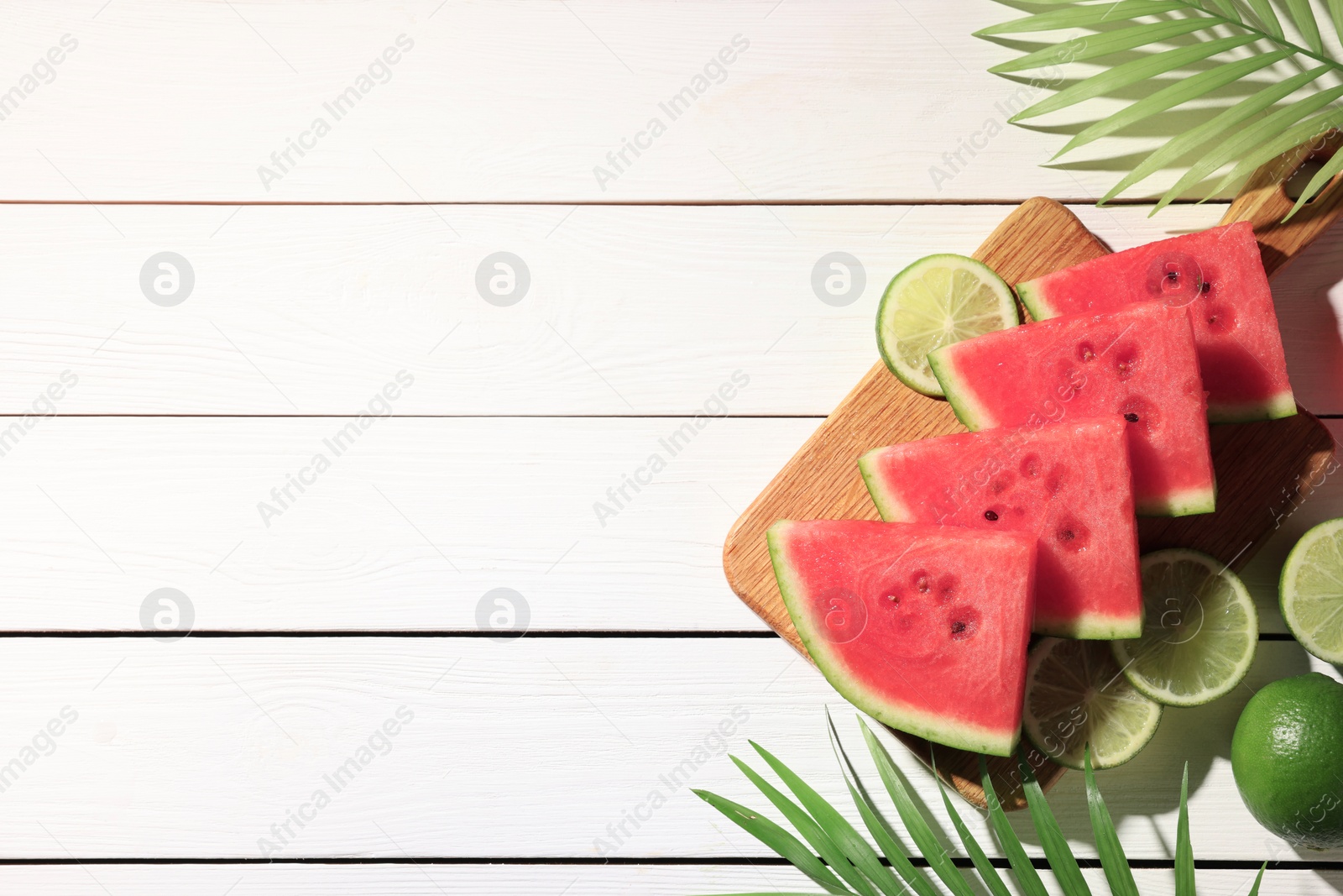 Photo of Tasty sliced watermelon and limes on white wooden table, flat lay. Space for text