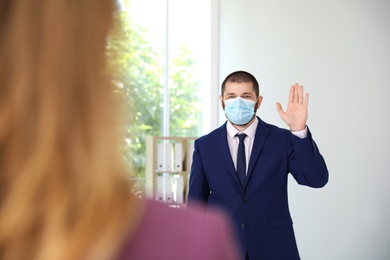Photo of Man in protective face mask saying hello in office. Keeping social distance during coronavirus pandemic