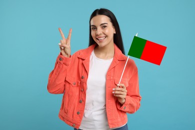 Image of Happy young woman with flag of Portugal showing V-sign on light blue background