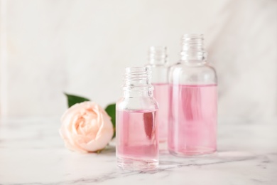 Bottles of essential oil and rose on marble table