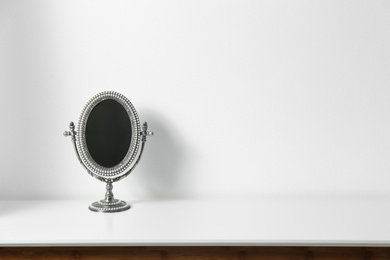 Small mirror on table near white wall. Space for text