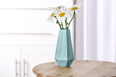 Beautiful tender chamomile flowers in vase on wooden table indoors