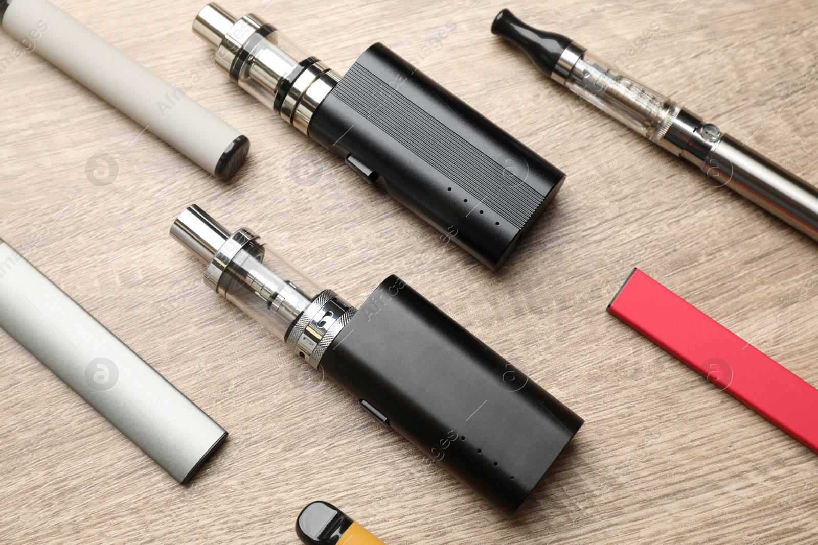 Photo of Different electronic cigarettes on wooden table, flat lay. Smoking alternative