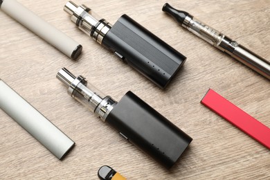 Different electronic cigarettes on wooden table, flat lay. Smoking alternative