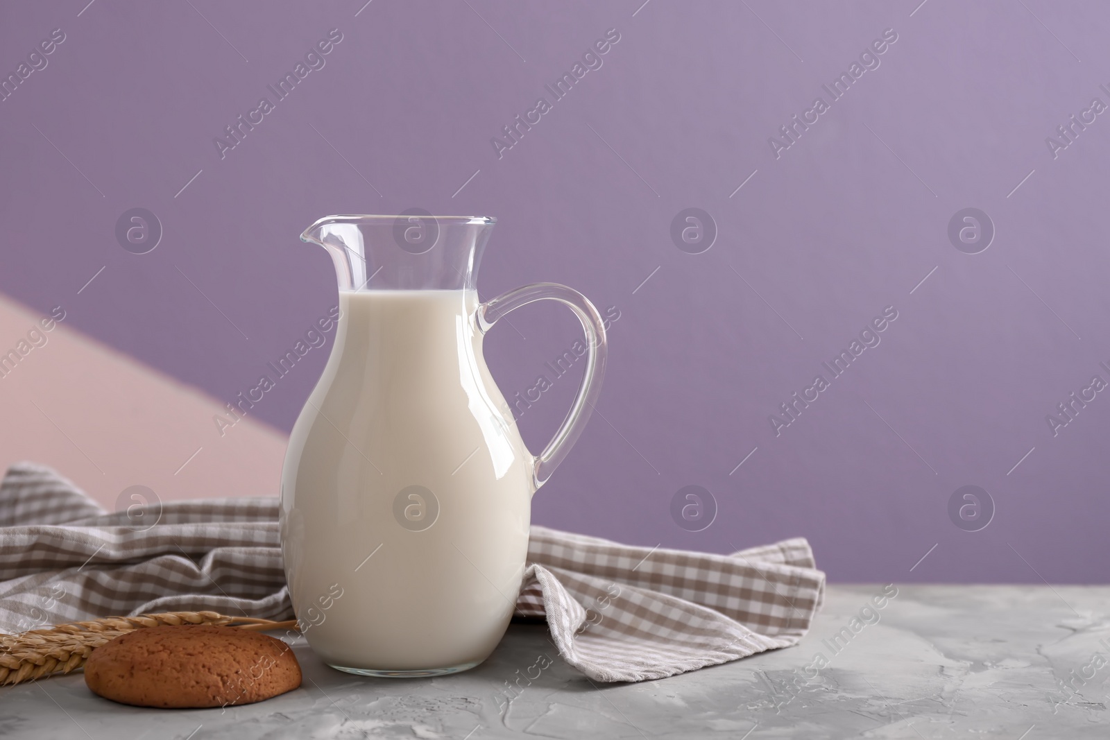 Photo of Jug of fresh milk and cookie on table against color background