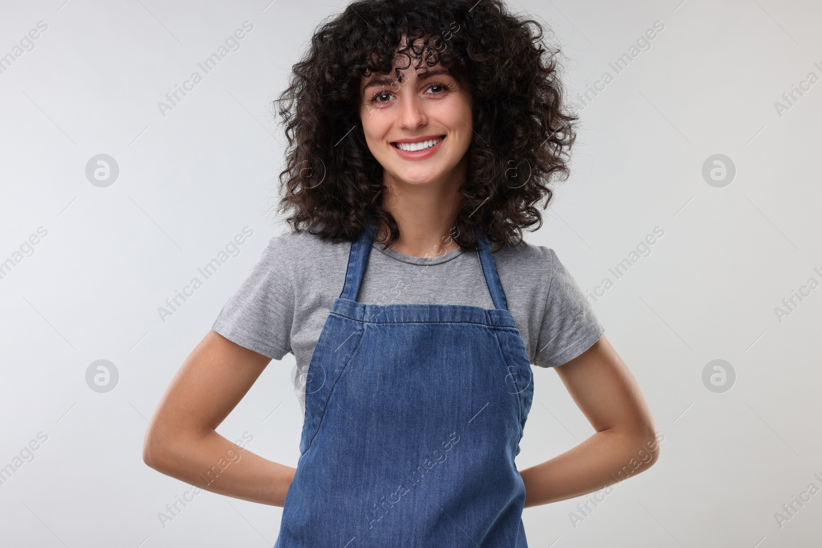 Photo of Happy woman wearing kitchen apron on light grey background. Mockup for design