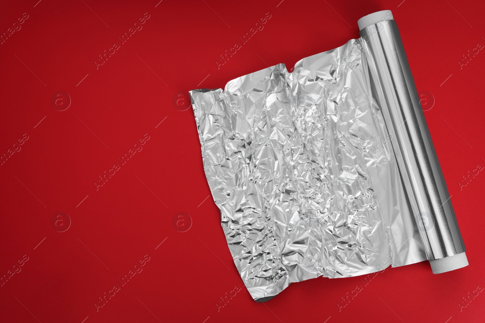 Photo of Roll of aluminum foil on red background, top view. Space for text