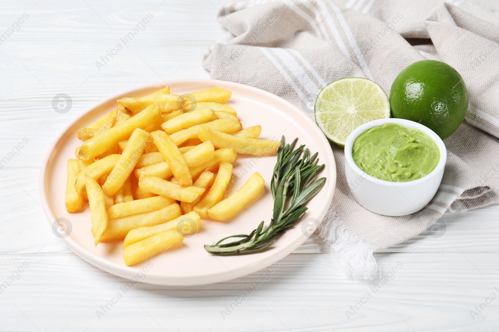 Photo of Plate with french fries, avocado dip, rosemary and lime served on white wooden table