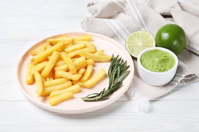 Photo of Plate with french fries, avocado dip, rosemary and lime served on white wooden table