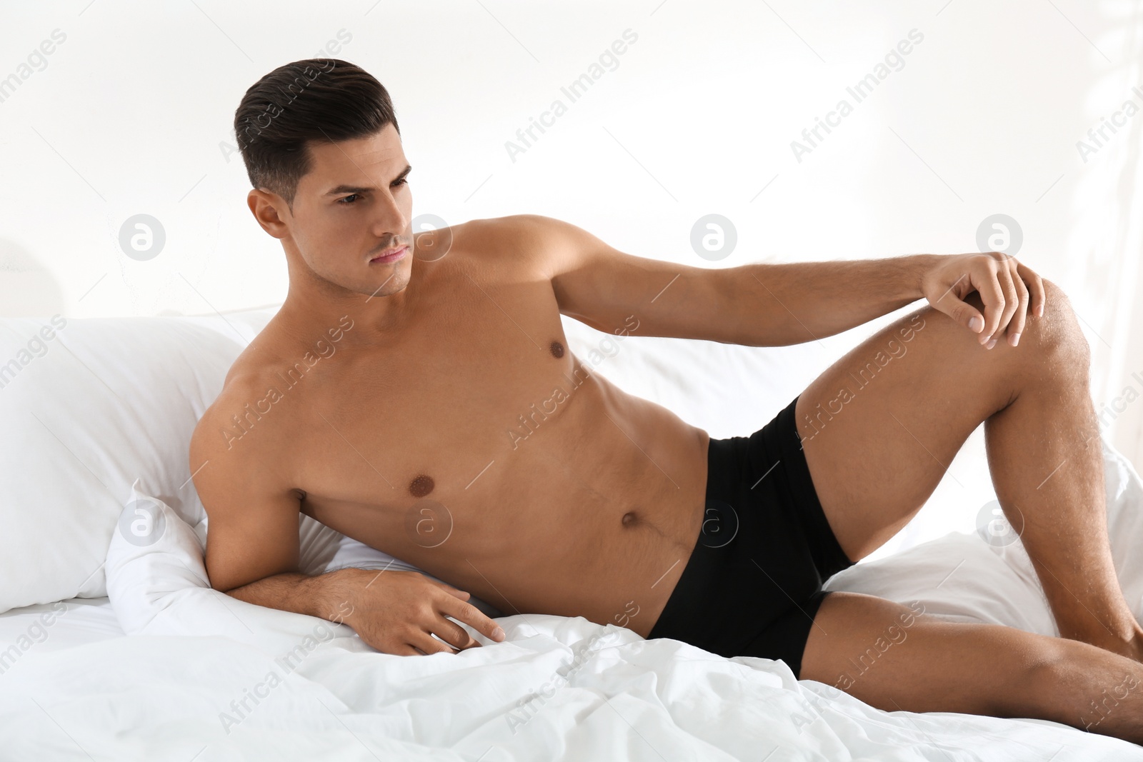 Photo of Handsome man in black underwear on bed indoors