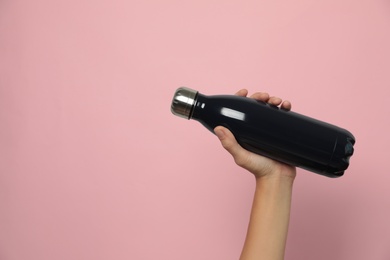 Woman holding modern dark thermos on pink background, closeup. Space for text