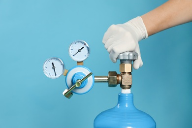 Photo of Medical worker checking oxygen tank on light blue background, closeup