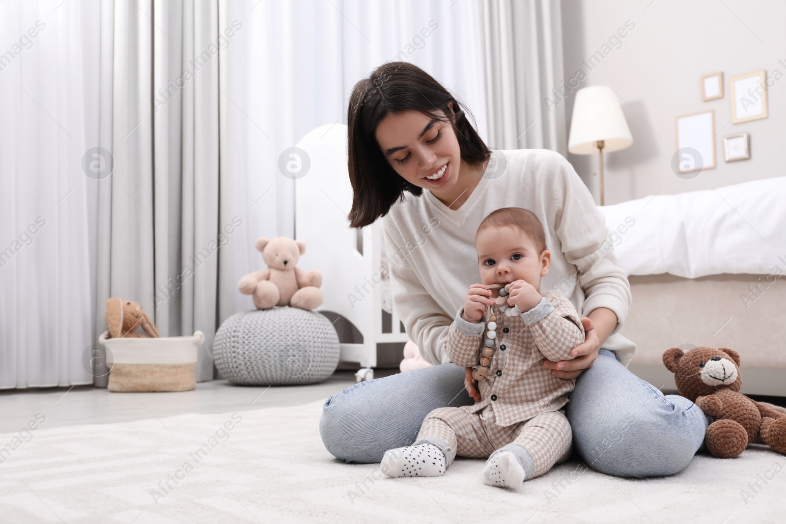 Photo of Young mother and her baby with teether on floor at home. Space for text