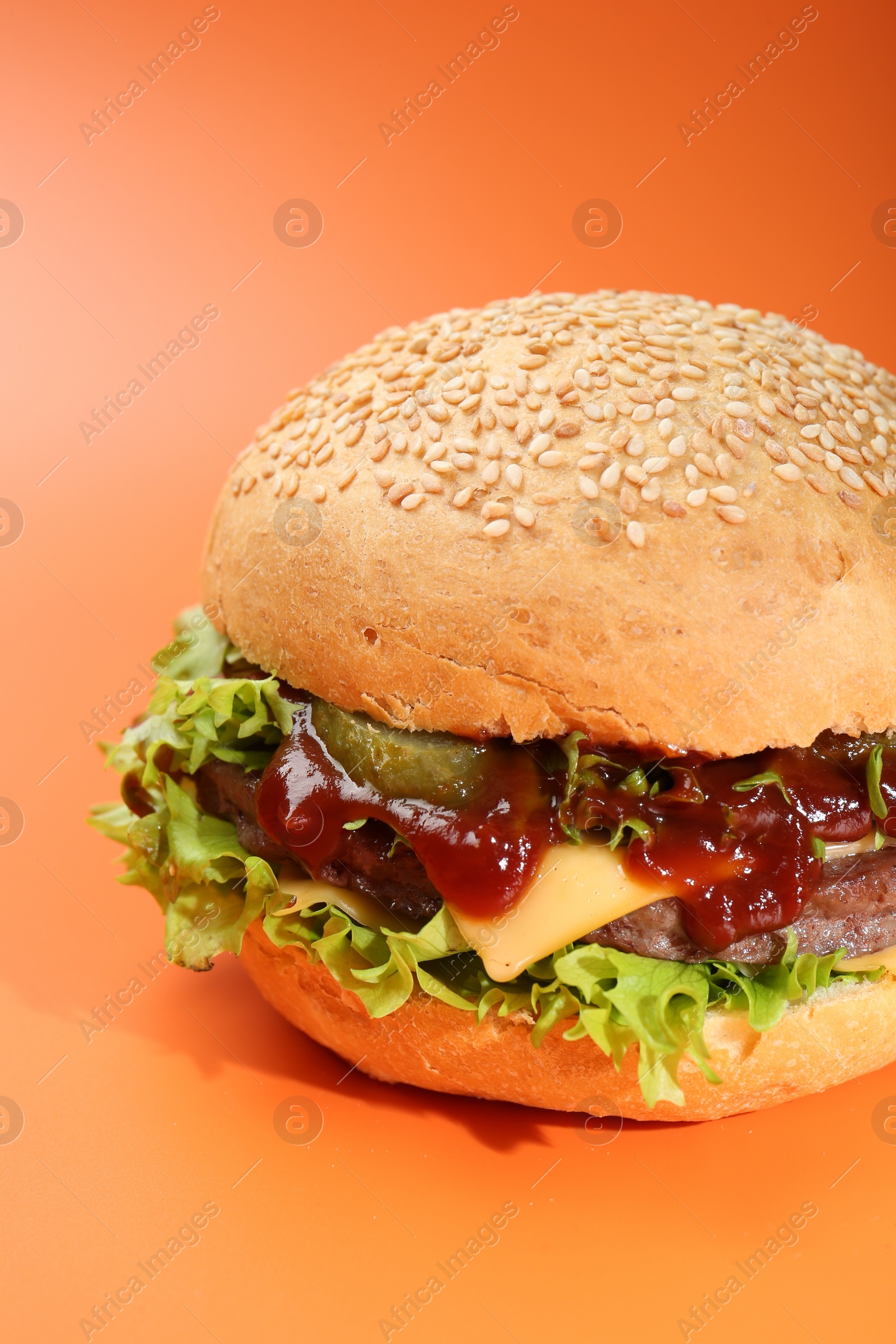 Photo of Delicious cheeseburger with lettuce, pickle, ketchup and patty on coral background, closeup