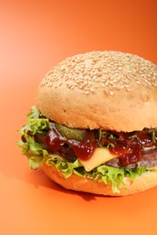 Photo of Delicious cheeseburger with lettuce, pickle, ketchup and patty on coral background, closeup