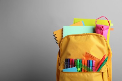 Yellow backpack with different school stationery on grey background, space for text