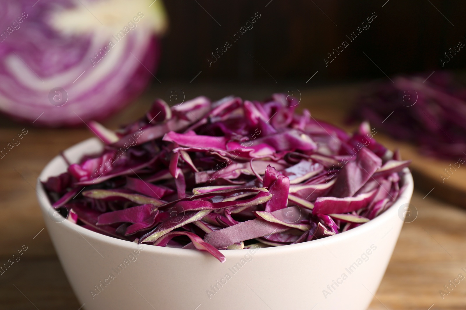 Photo of Fresh chopped red cabbage in bowl on wooden table, closeup