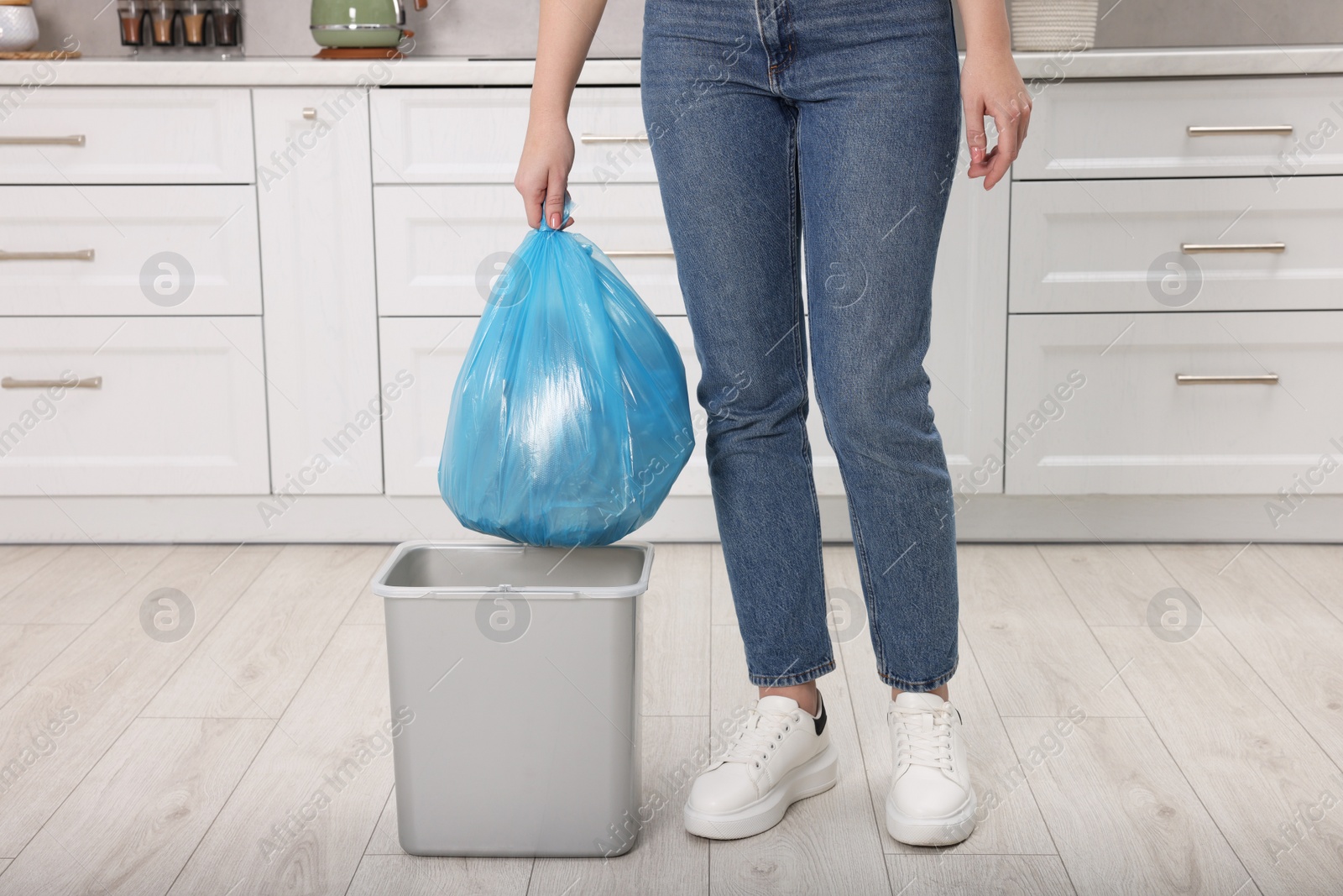 Photo of Woman taking garbage bag out of trash bin in kitchen, closeup