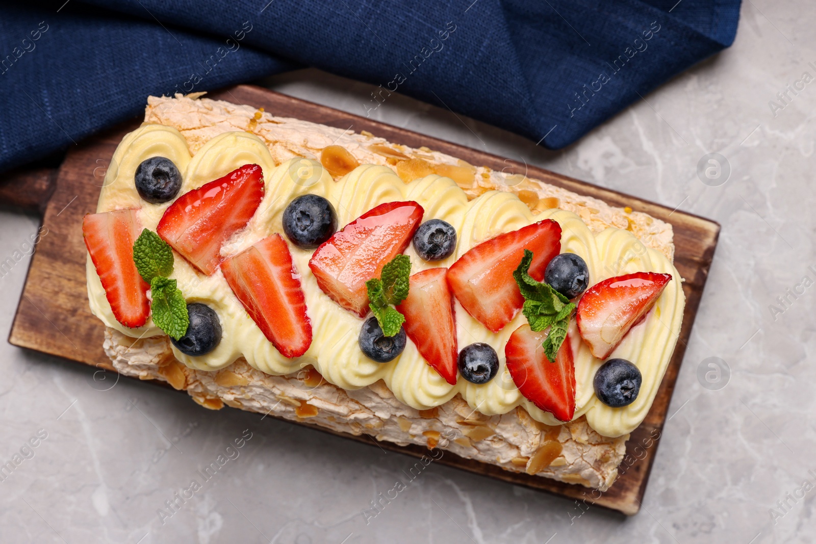 Photo of Tasty meringue roll with cream, strawberry, blueberry and mint on light grey marble table, top view