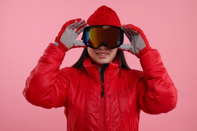 Happy woman in winter sportswear and goggles on pink background
