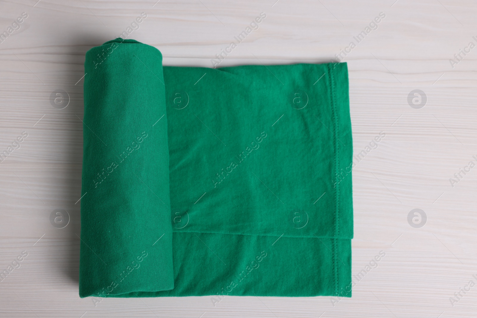 Photo of Sorting and organizing. Rolled green garment on white wooden table, top view