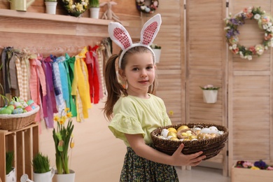 Adorable little girl with bunny ears and basket full of dyed eggs in Easter photo zone