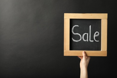 Closeup view of woman holding chalkboard with word Sale against dark background, space for text. Black Friday concept