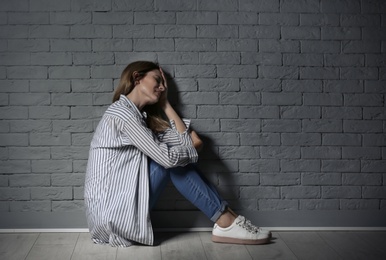 Lonely woman suffering from depression near brick wall