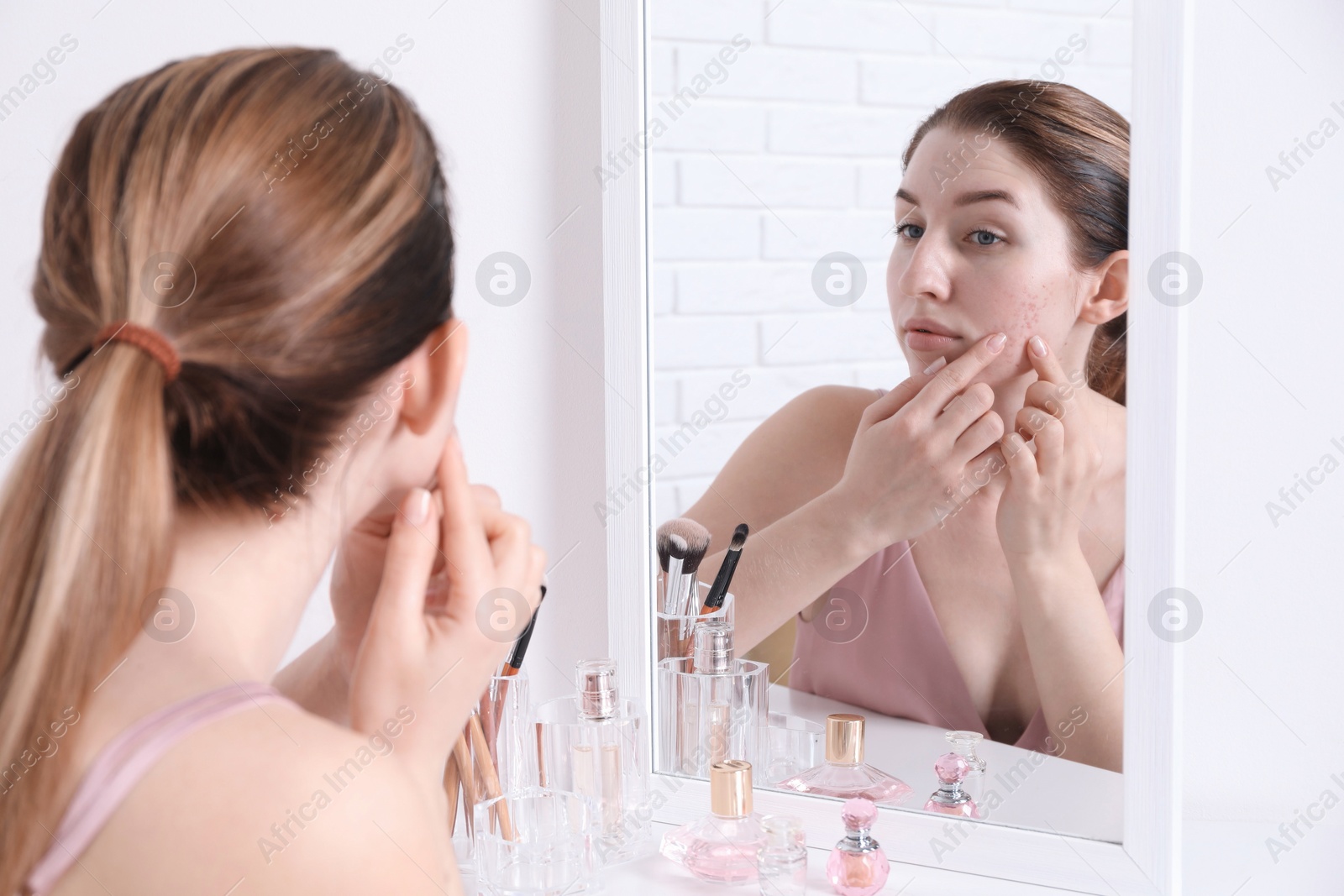 Photo of Woman with acne problem near mirror indoors