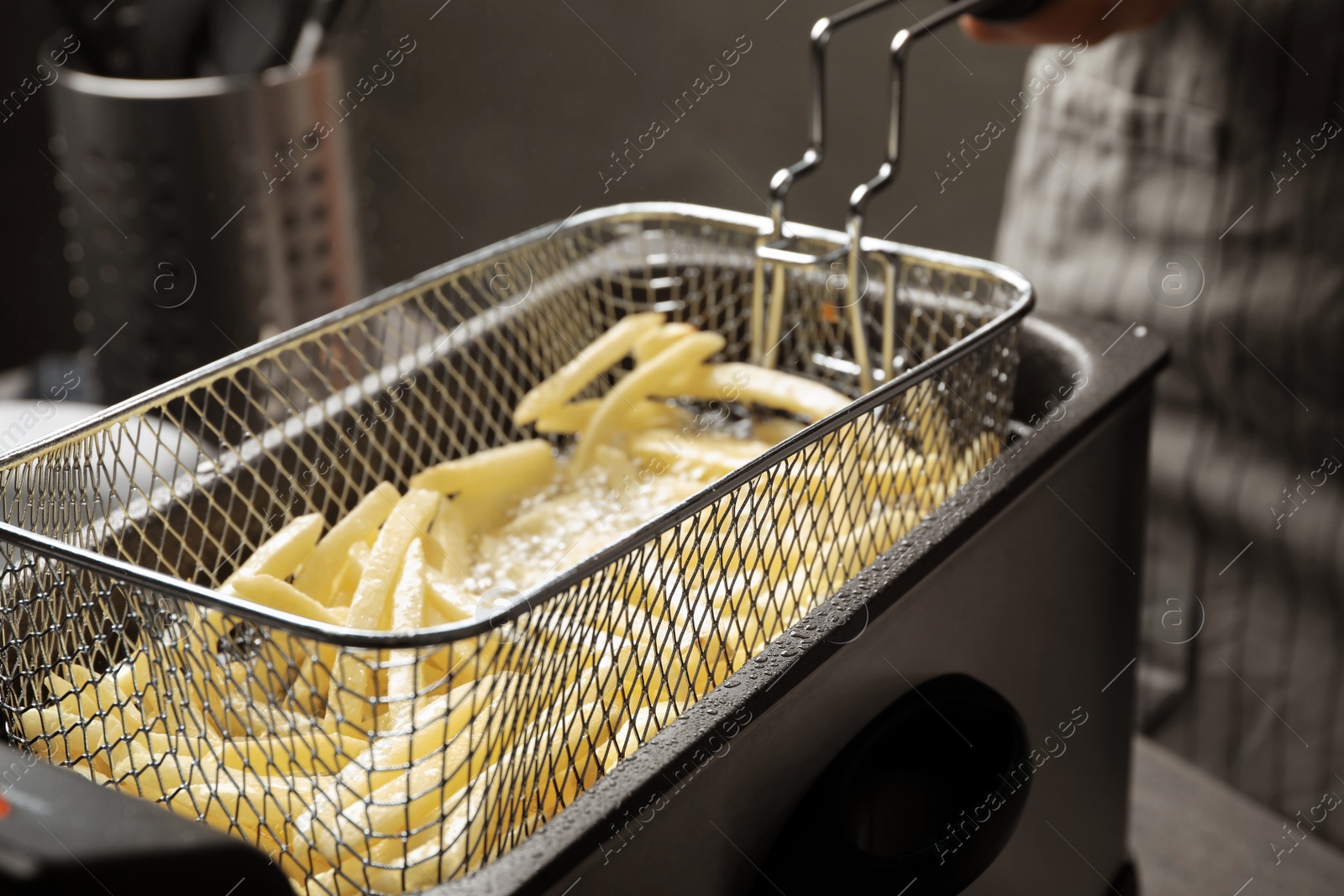 Photo of Cooking delicious french fries in hot oil, closeup