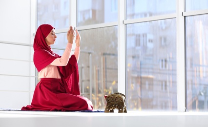 Photo of Muslim woman in hijab praying on mat indoors. Space for text