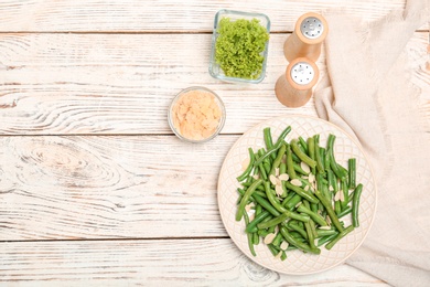 Photo of Plate with tasty green beans and almonds on wooden table, top view