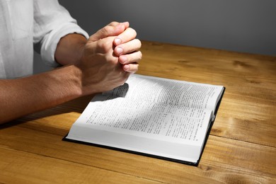 Photo of Man with Bible praying at wooden table, closeup
