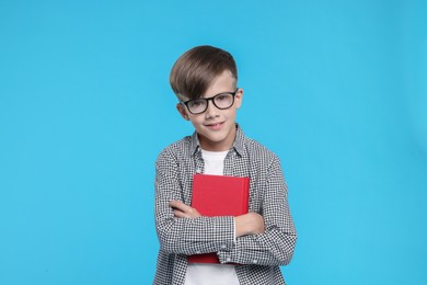Photo of Cute schoolboy in glasses with book on light blue background