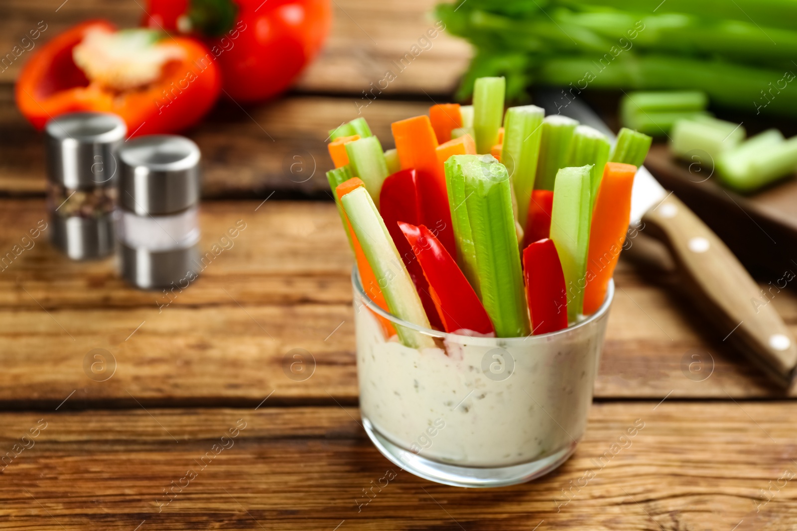 Photo of Celery and other vegetable sticks with dip sauce in glass bowl on wooden table