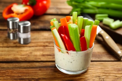 Photo of Celery and other vegetable sticks with dip sauce in glass bowl on wooden table