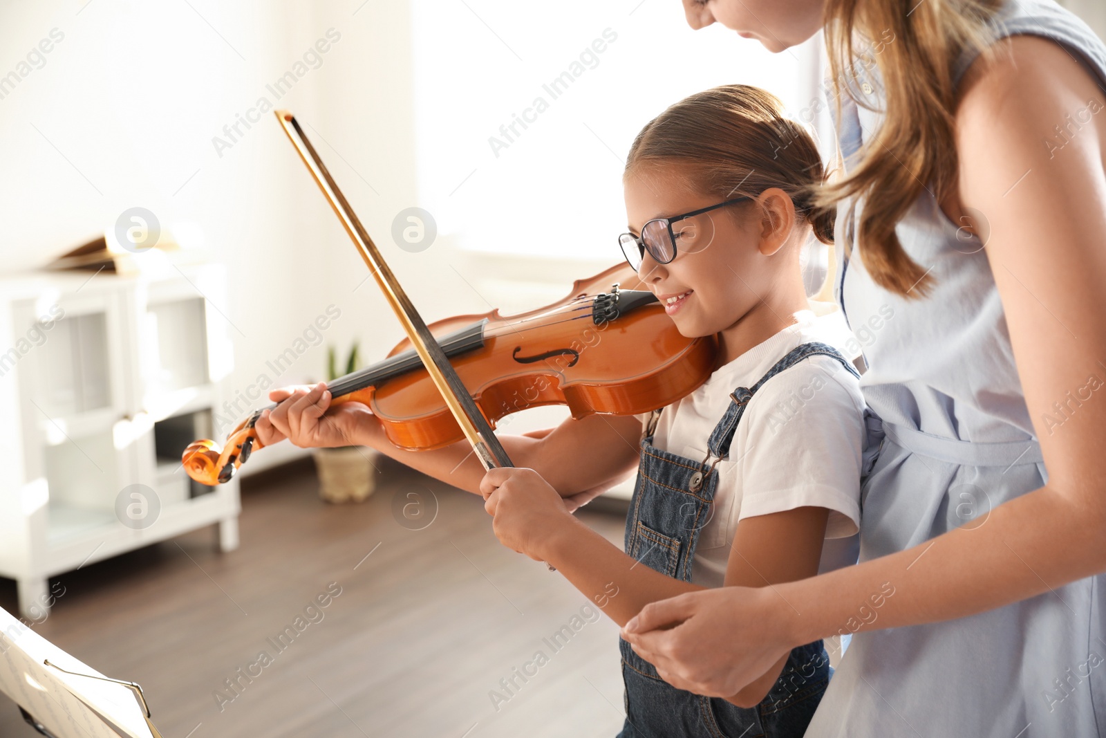 Photo of Young woman teaching little girl to play violin indoors