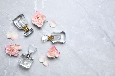Bottles of perfume and beautiful flowers on light grey background, flat lay. Space for text