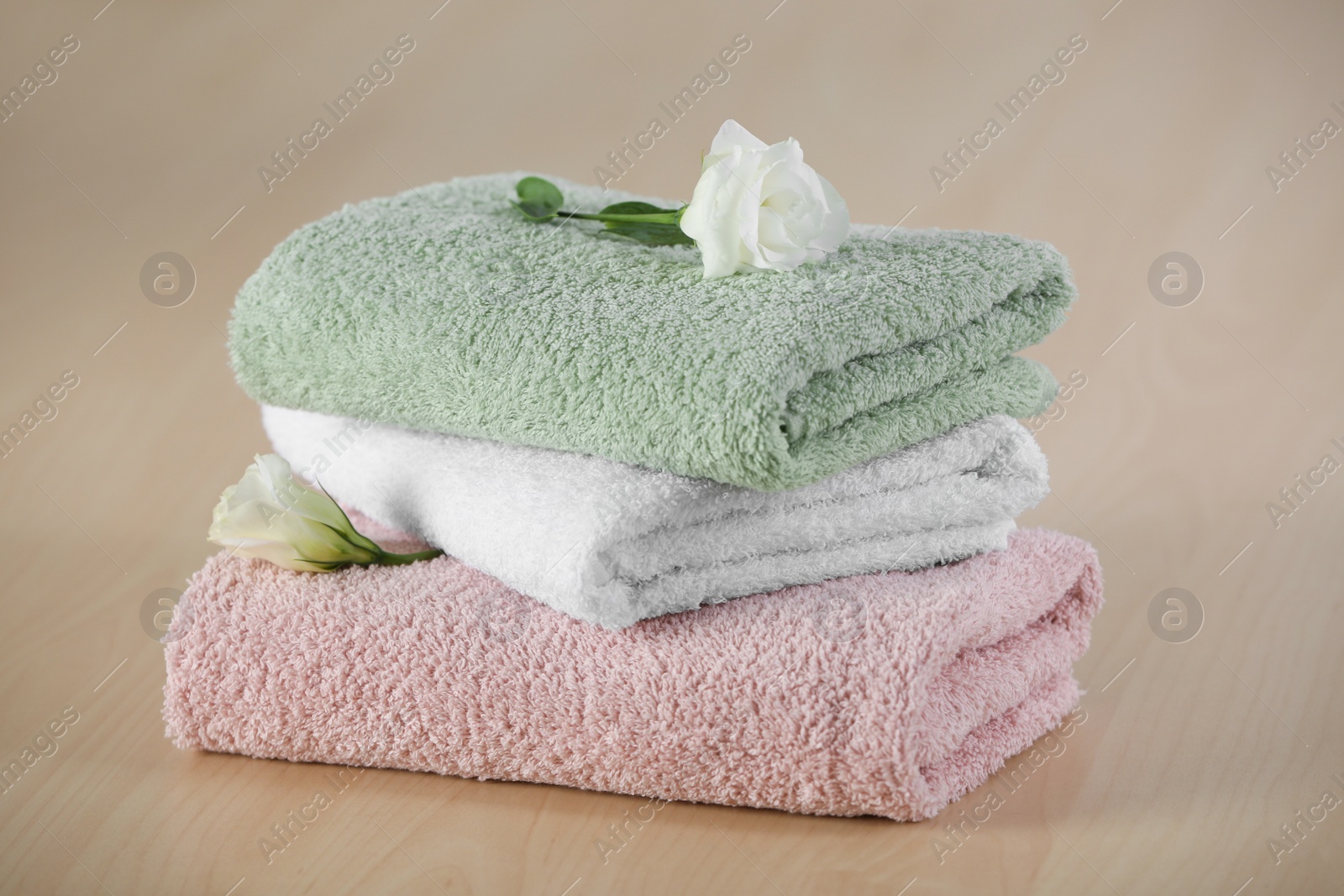 Photo of Soft folded towels with eustoma flowers on wooden table